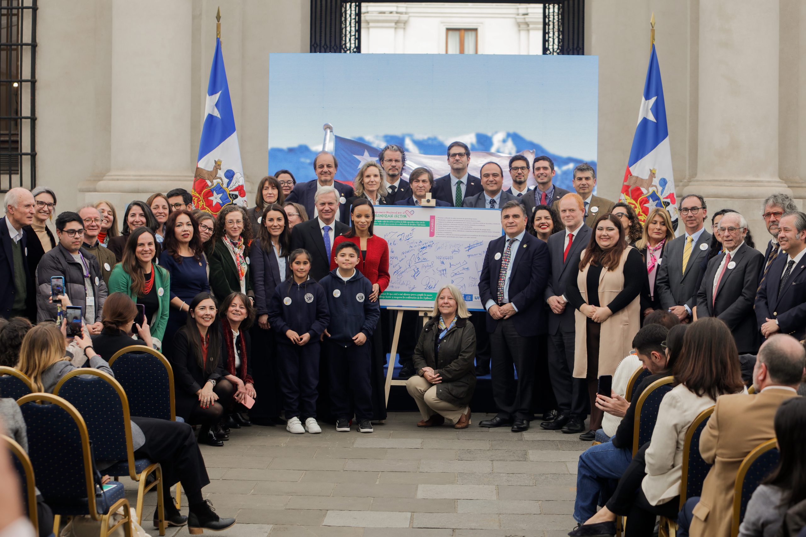 Autoridades, docentes y estudiantes junto al panel firmado del Compromiso Nacional por el Aprendizaje Lector en La Moneda